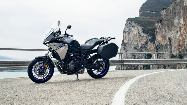 Una motocicleta está estacionada al costado de una carretera al lado de una montaña.