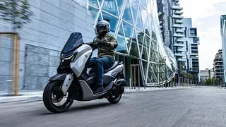 Un hombre va conduciendo una scooter por una calle de la ciudad.