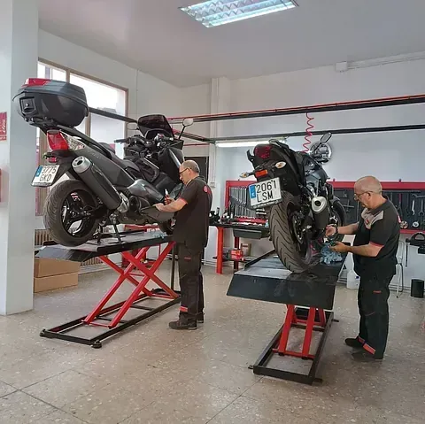 Dos hombres están trabajando en una motocicleta en un garaje.