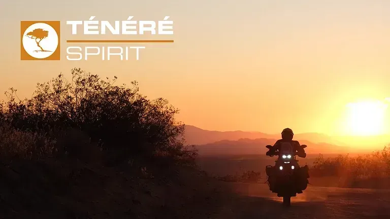 Una persona conduce una motocicleta por un camino de tierra al atardecer.