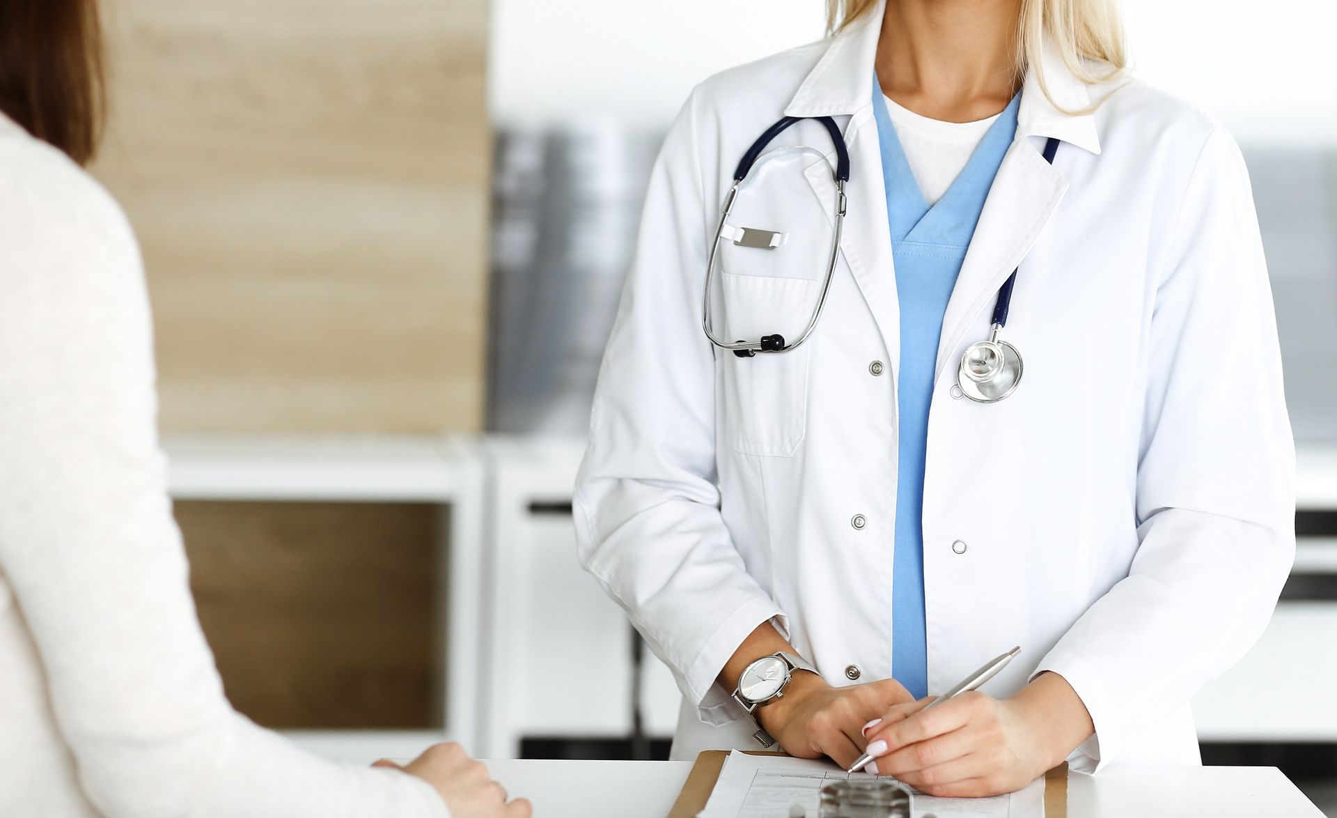 Médico con bata blanca y estetoscopio consultando a un paciente.