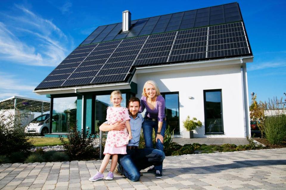 Familie vor einem Haus mit Solarpaneln auf dem Dach