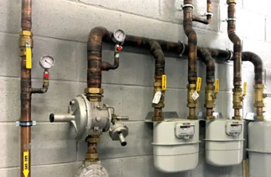 Una fila de medidores de gas conectados a tuberías de cobre en una pared.