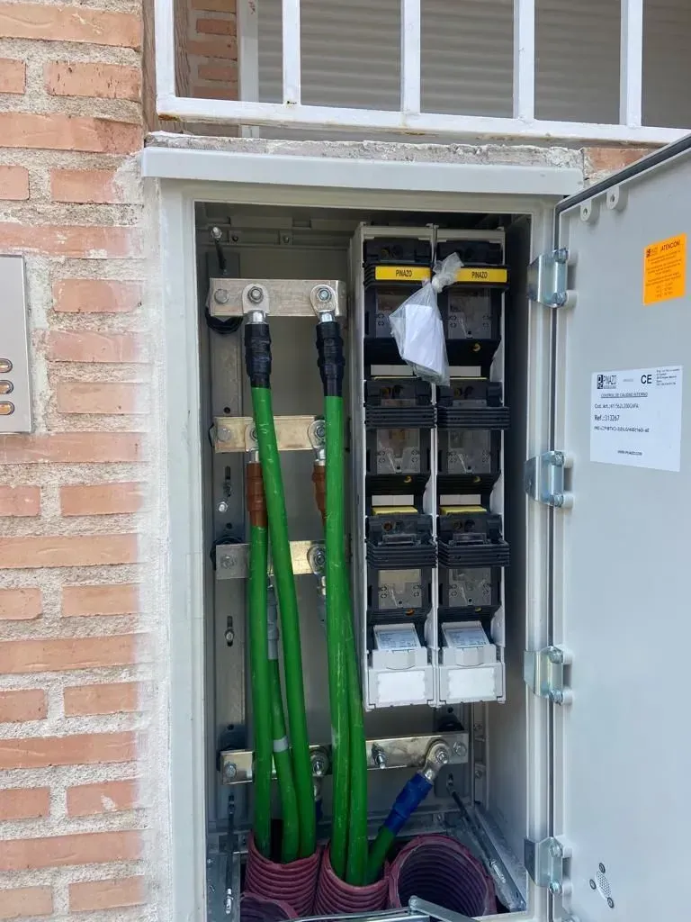 Una caja eléctrica con cables verdes que salen de ella está colocada sobre una pared de ladrillos.