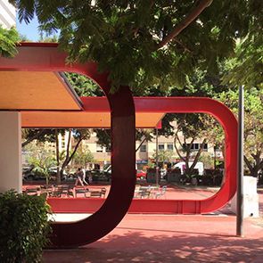 Una escultura roja en un parque con árboles al fondo.
