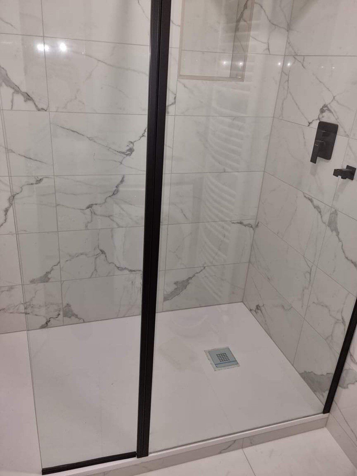 Cabinet de douche avec carrelage blanc effet marbre.