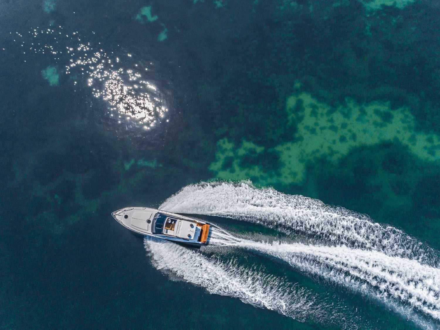 Un barco avanza a toda velocidad sobre el agua azul oscuro, creando una estela blanca, con la luz del sol reflejándose en la superficie.