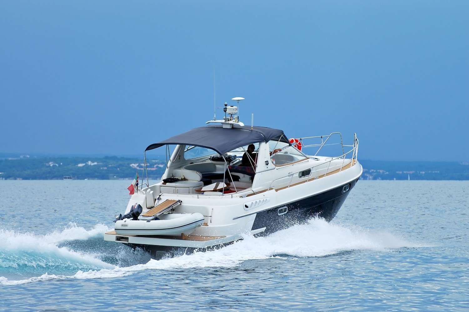 Lancha a motor navegando a toda velocidad, creando una estela. Casco blanco y azul oscuro, con una cubierta oscura. Cielo y mar azules.