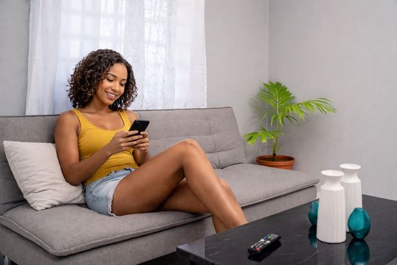 Woman relaxing on a gray sofa, looking at her phone beside a coffee table with decor at Chenko Villas + Rental Cars