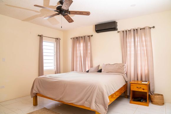 Neat bedroom with a made bed, ceiling fan, curtained windows, and a small bedside table at Chenko Villas + Rental Cars