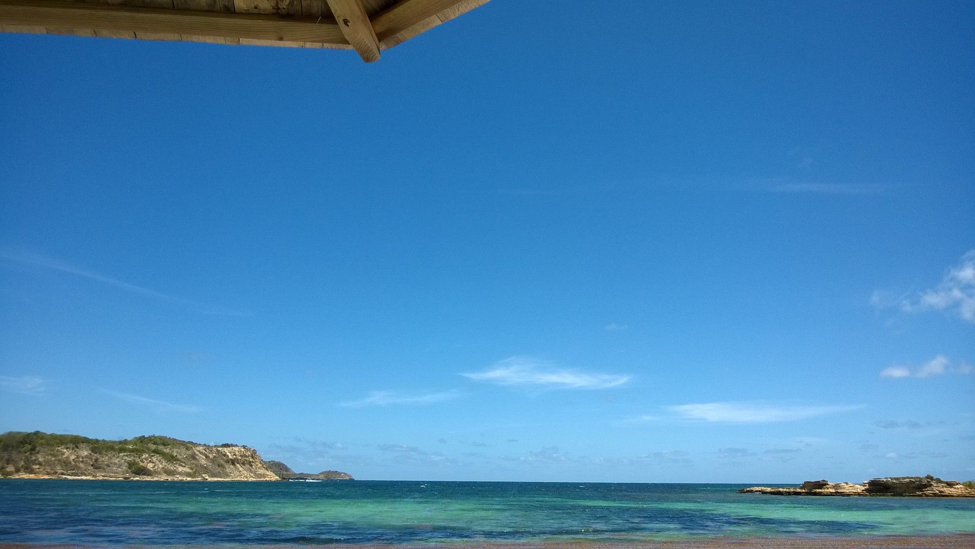 Tropical beach with clear blue sky, turquoise water, and a rocky shoreline in Antigua.