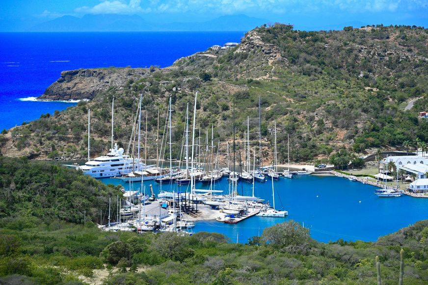 Marina with sailboats in a turquoise bay, surrounded by green hills under a clear blue sky in English Harbor, Antigua.