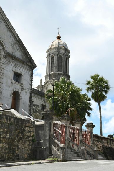 Stone church tower behind a wall and trees under a bright sky in Antigua.