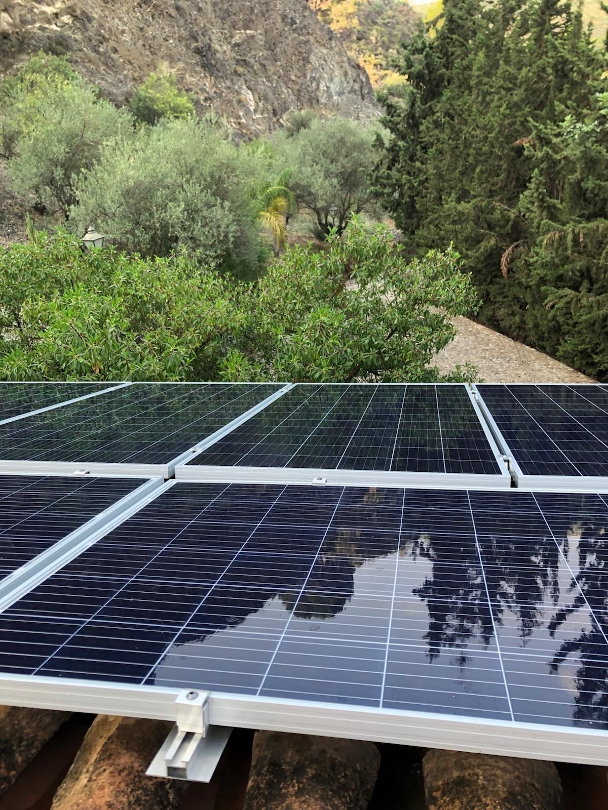 Paneles solares sobre un techo de terracota con un exuberante fondo de montaña verde.