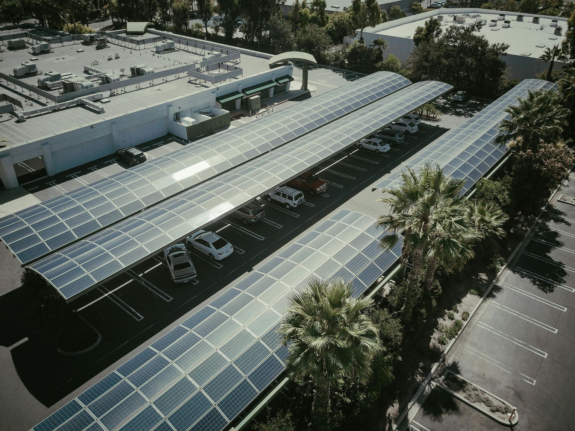 Paneles solares sobre plazas de estacionamiento en un edificio comercial, proporcionando sombra.