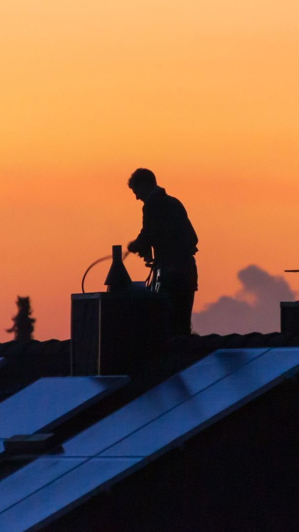 Homme sur un toit en train de ramoner une cheminée au coucher du soleil