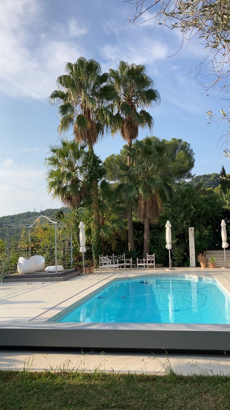 Piscine extérieure avec palmiers et chaises longues sous un ciel bleu azur