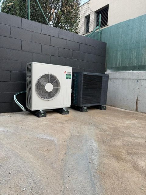 Dos unidades de aire acondicionado sobre hormigón junto a una pared pintada de negro.