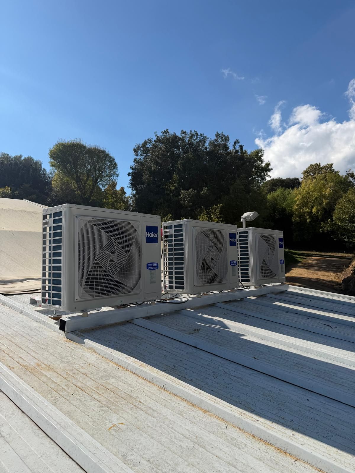 Cuatro unidades de aire acondicionado Carrier sobre un techo metálico, cielo azul, árboles al fondo.