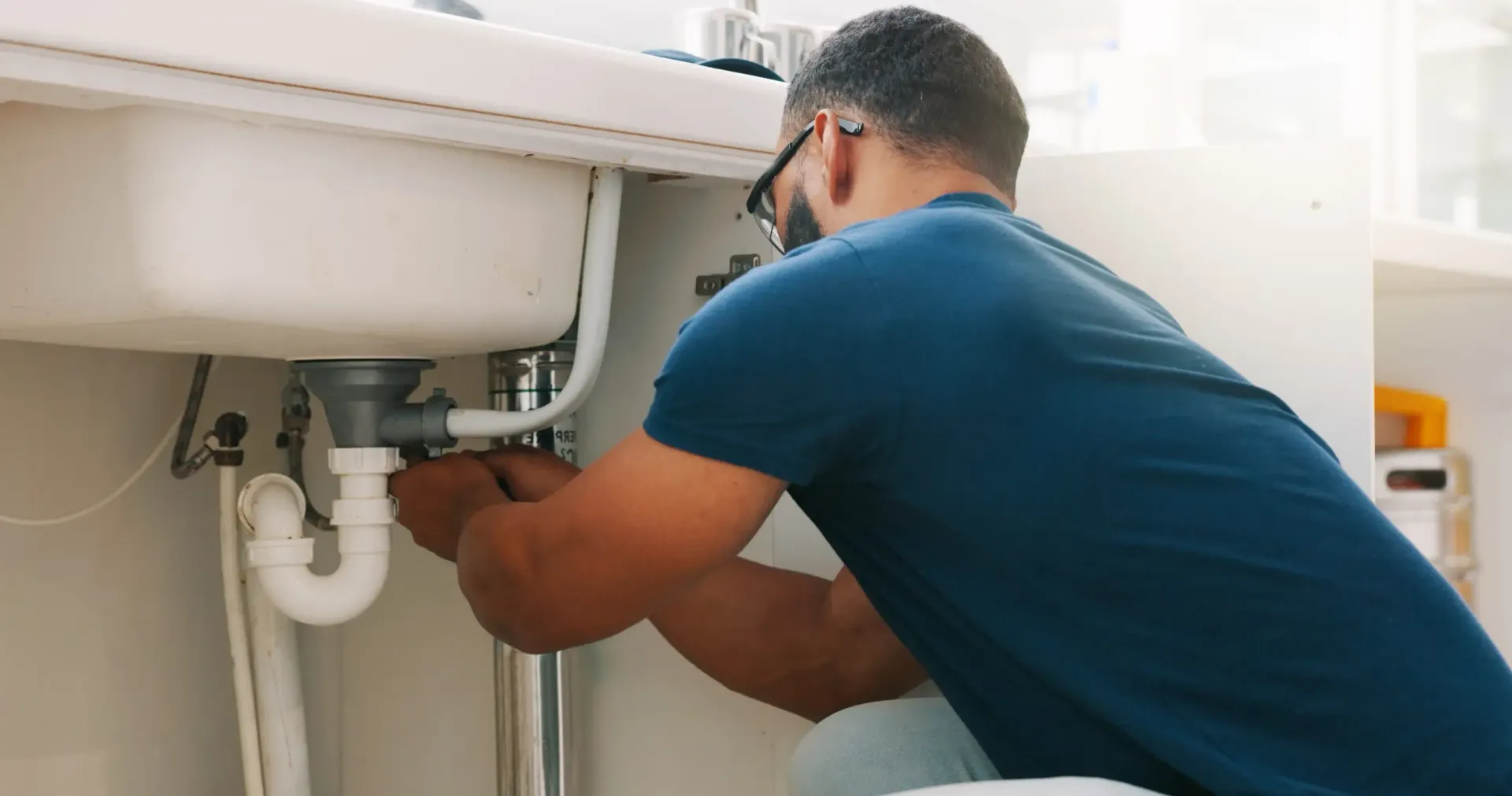 Un hombre arregla las tuberías debajo del lavabo de un baño con una llave inglesa.