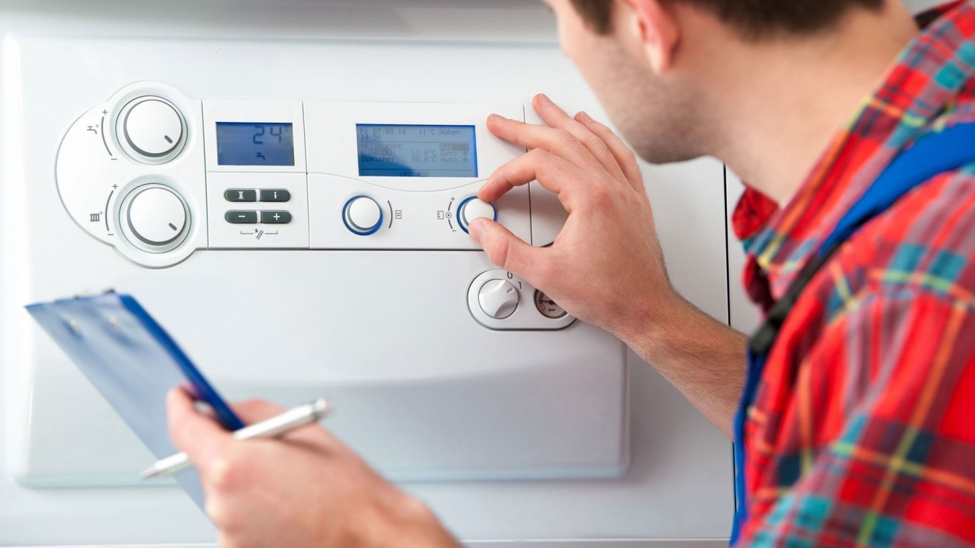 Persona ajustando un termostato de pared blanco mientras sostiene un teléfono inteligente y un bolígrafo.