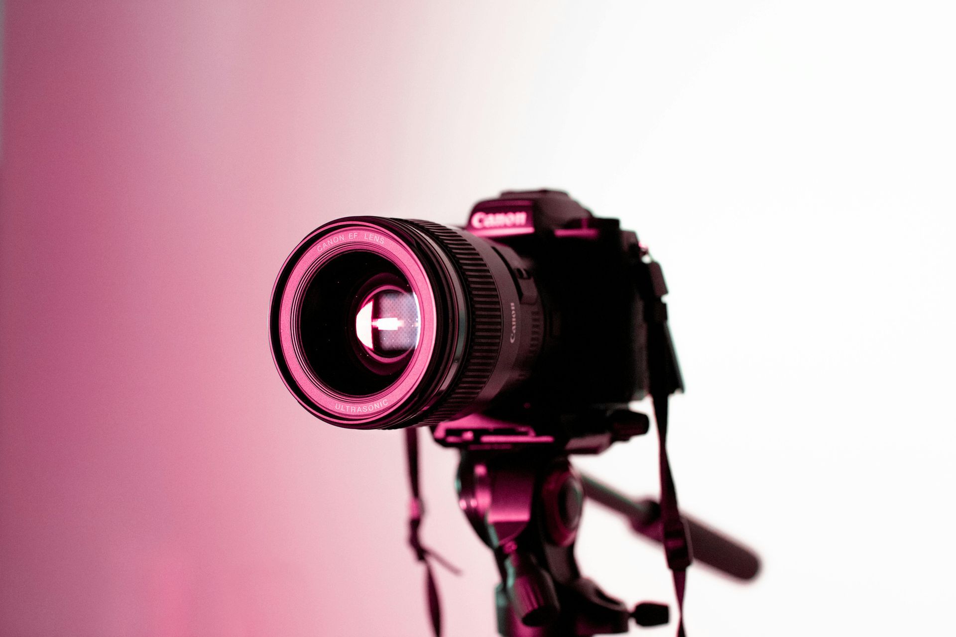 A close up of a camera on a tripod on a pink background.