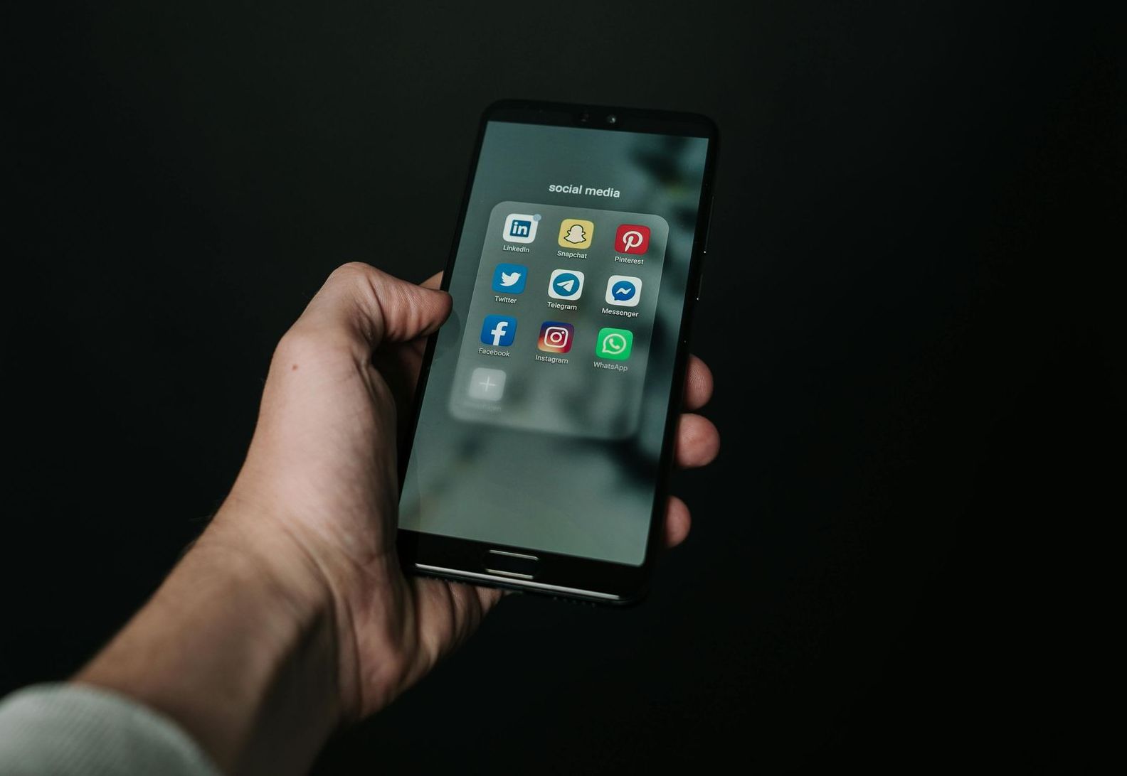 A person is holding a cell phone with social media icons on the screen.