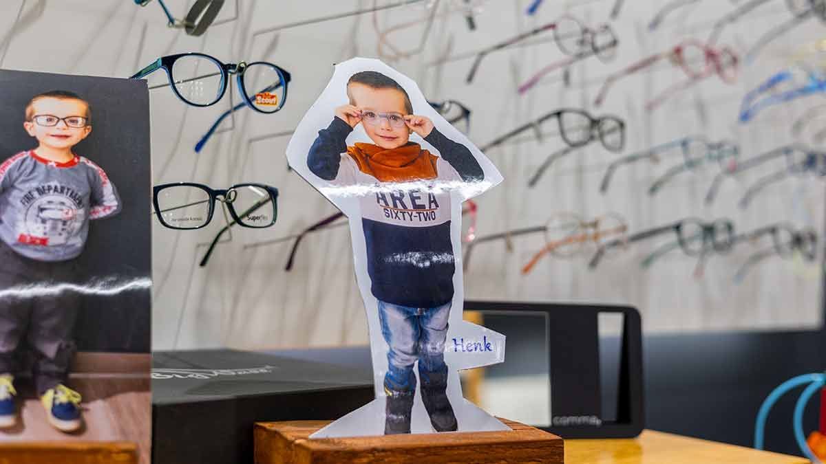 Auf einem Tisch sitzt die Pappfigur eines kleinen Jungen mit Brille.