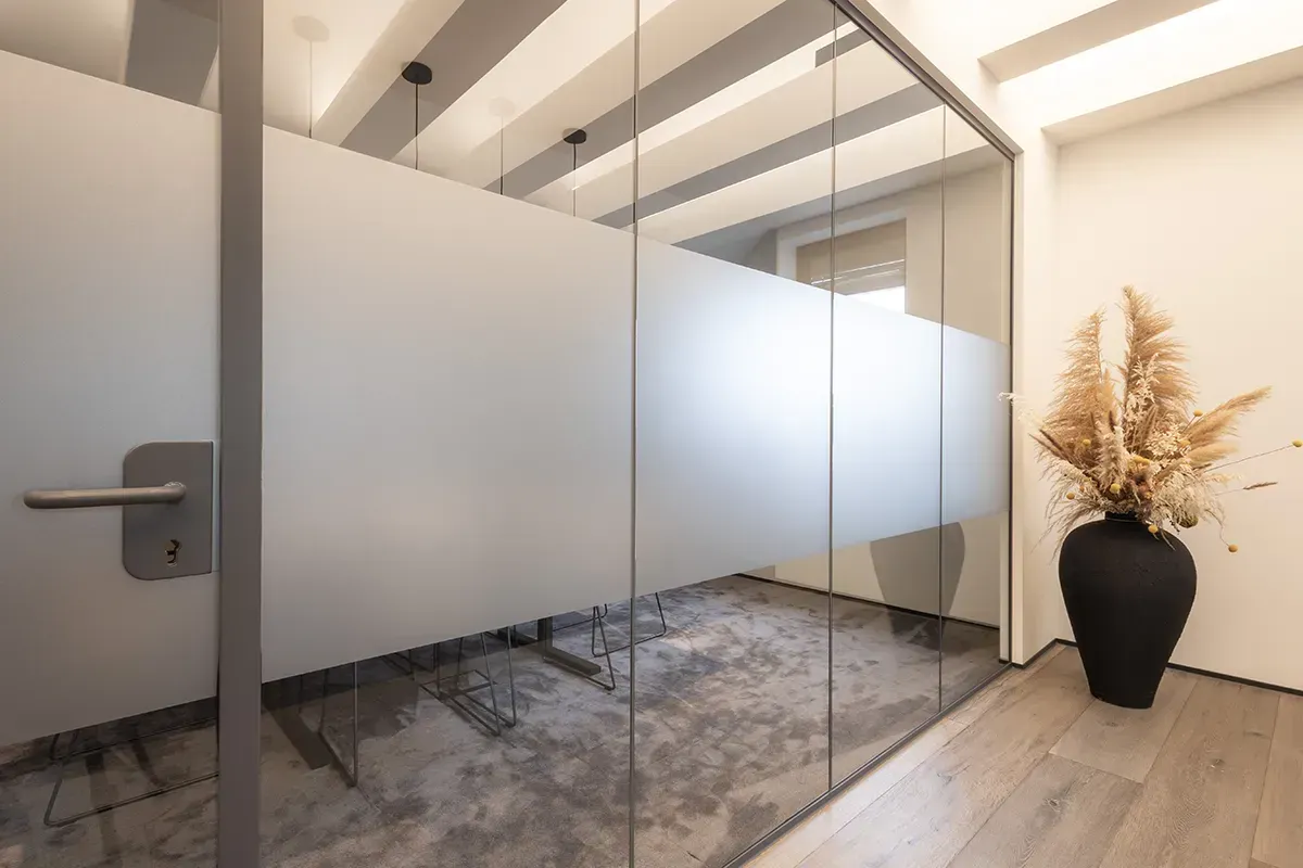 Ein Raum mit einer Glaswand und einer Vase mit Blumen auf dem Boden.