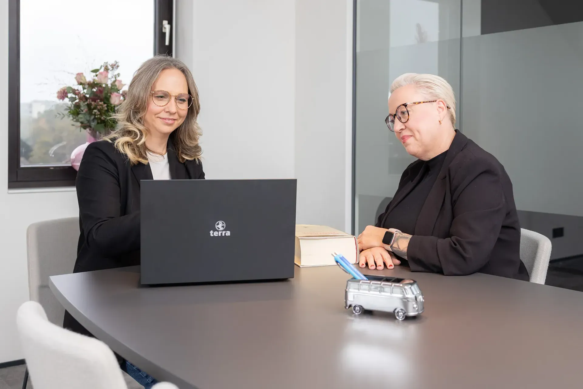 Zwei Frauen sitzen mit einem Laptop an einem Tisch.