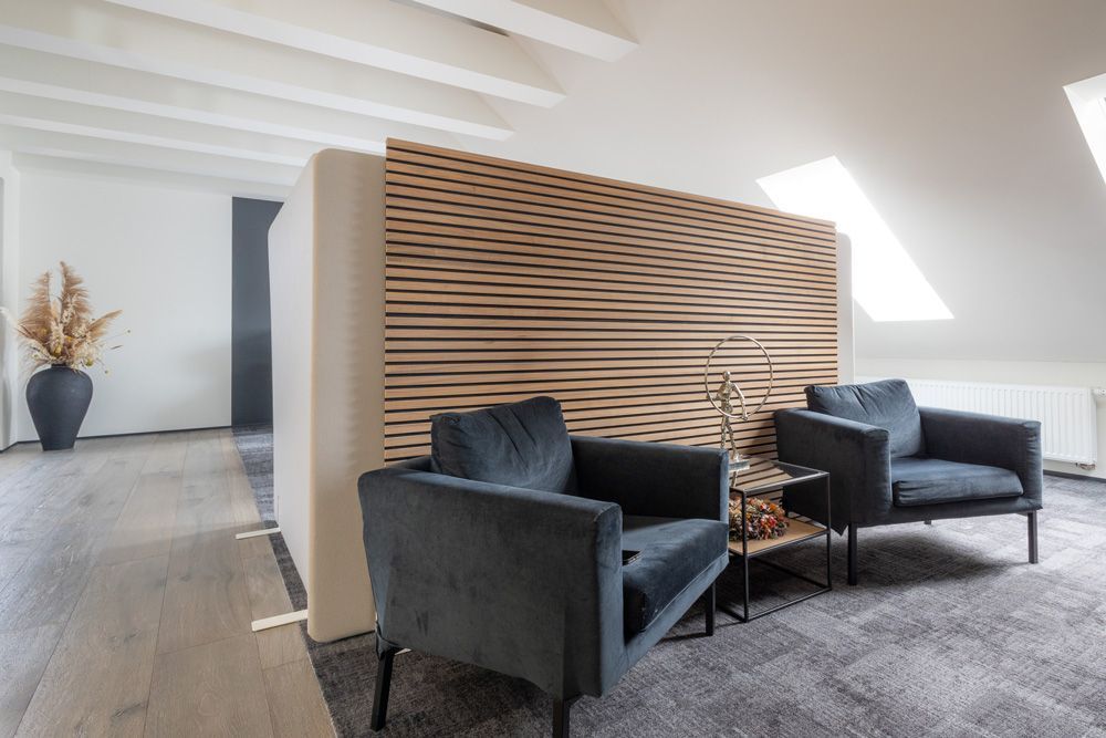 Zwei blaue Sessel stehen vor einer Holzlattenwand. Links davon steht eine Vase mit Pampasgras.