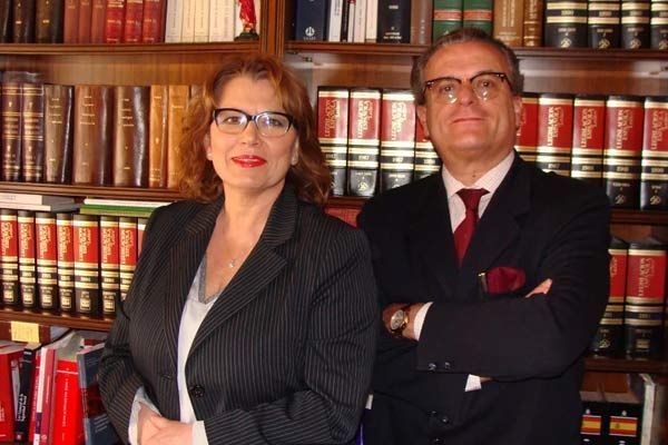 Dos profesionales con traje de pie frente a estanterías en una biblioteca jurídica.