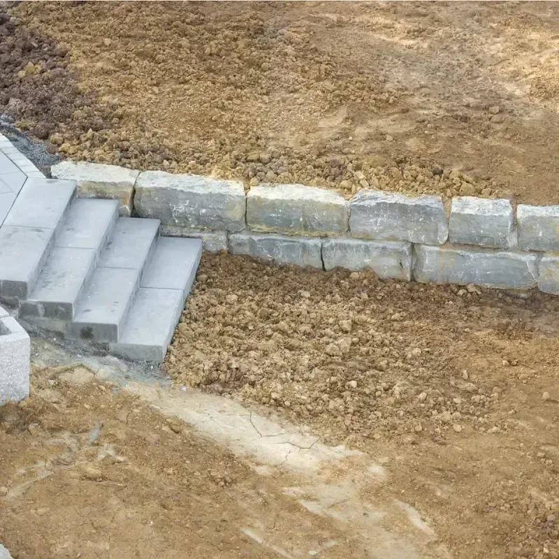 Bauarbeiten von Betonstufen neben einer niedrigen Stein-Stützmauer