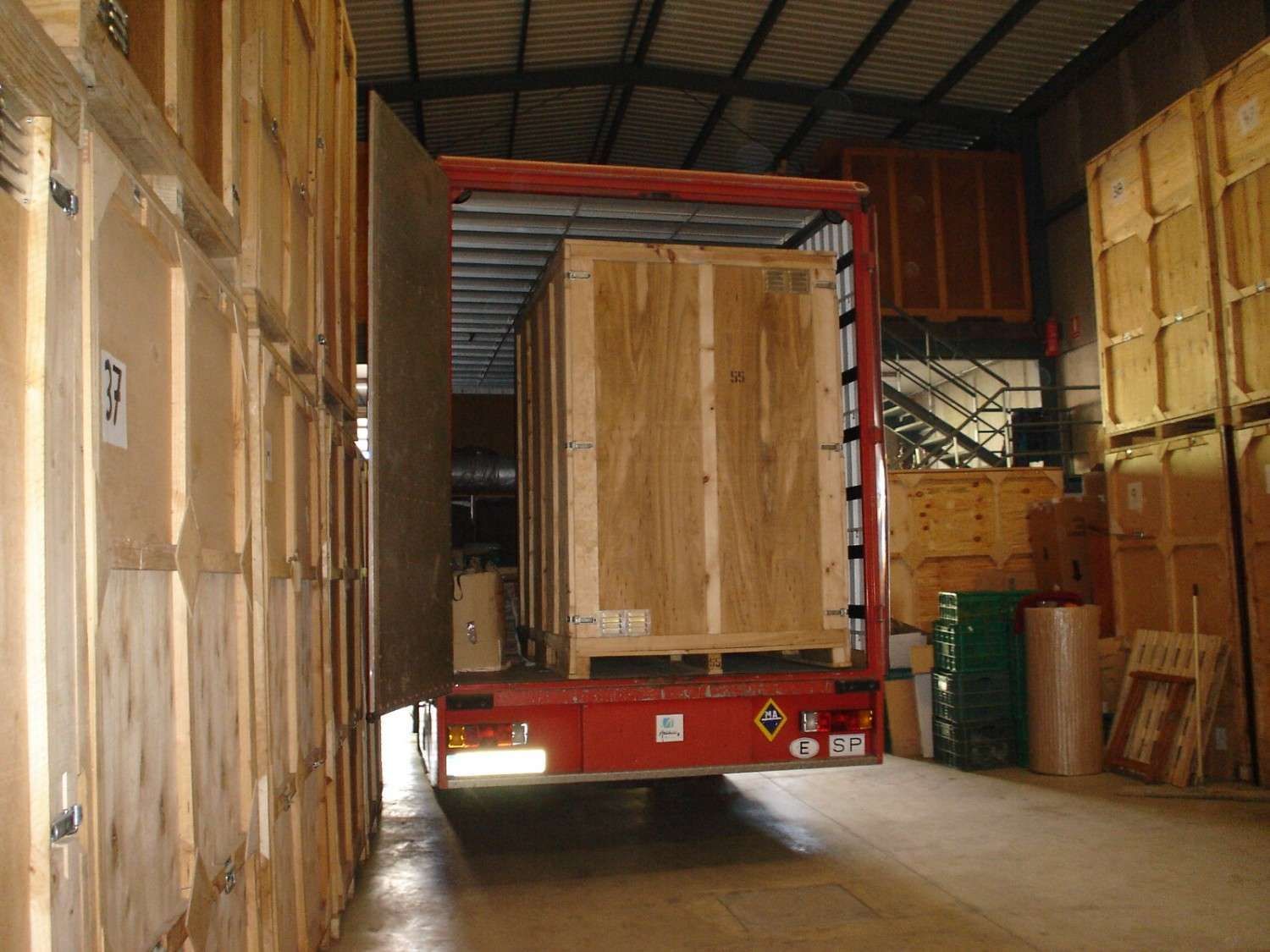 Un camión con remolque rojo cargado de cajas de madera se encuentra dentro de un almacén.