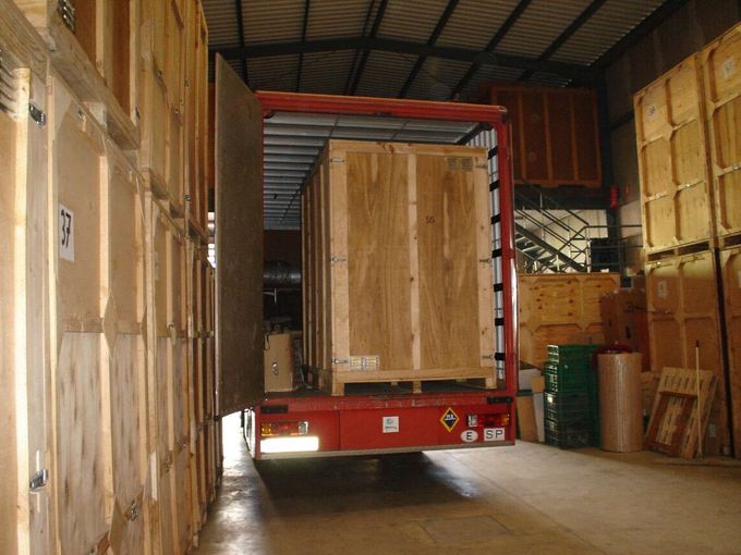 Un camión con remolque rojo cargado de cajas de madera se encuentra dentro de un almacén.