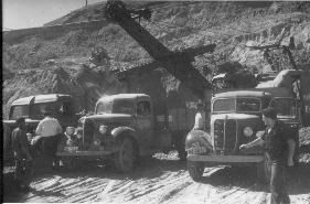 Una fotografía en blanco y negro de un grupo de camiones estacionados en un camino de tierra.