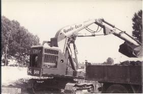Una fotografía en blanco y negro de una excavadora cargando tierra en un camión volquete.