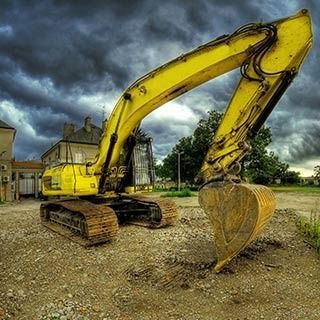 Una excavadora amarilla está sentada en un campo de tierra con un cielo nublado en el fondo.