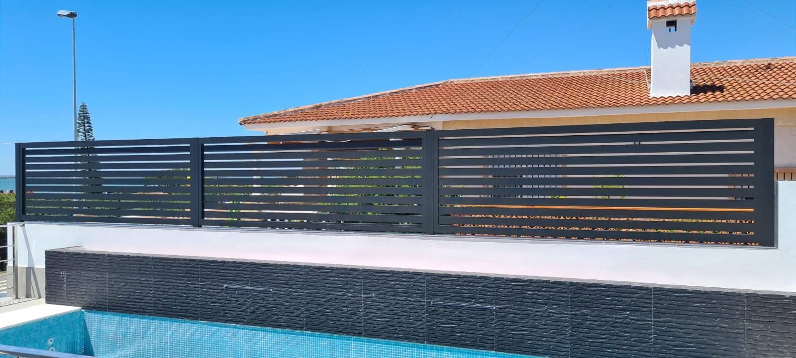 Una valla rodea una piscina delante de una casa.