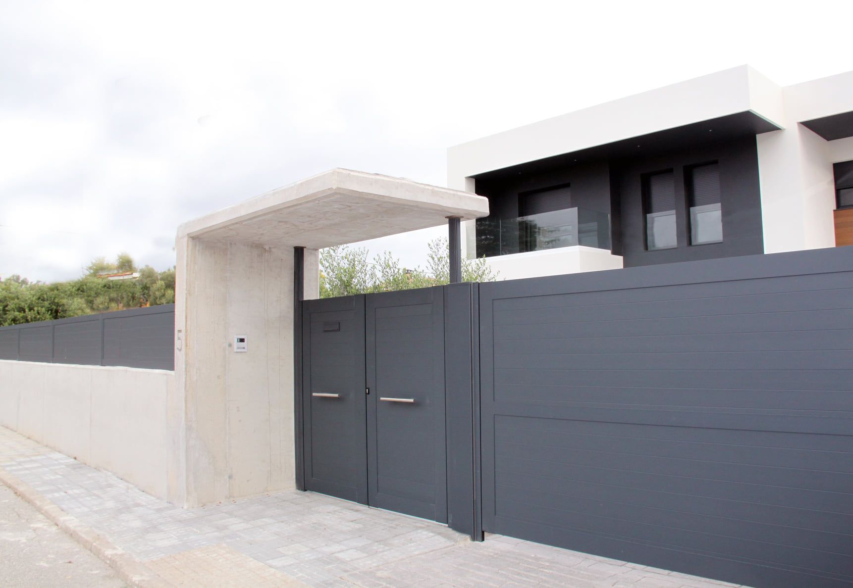 Una casa moderna con una valla gris y una puerta negra.