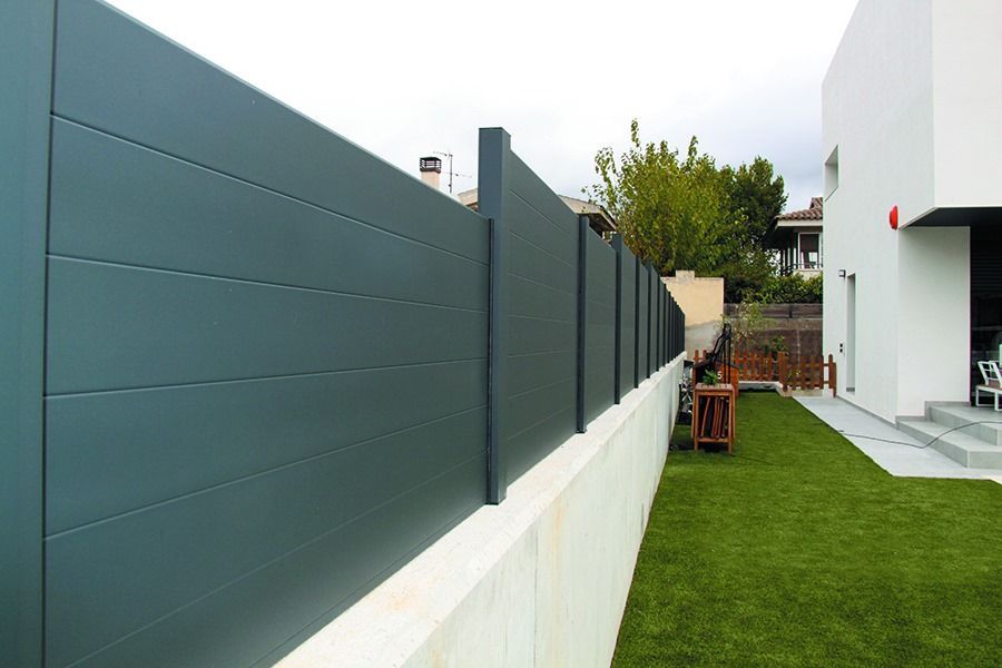 Una valla rodea un exuberante patio verde frente a una casa blanca.