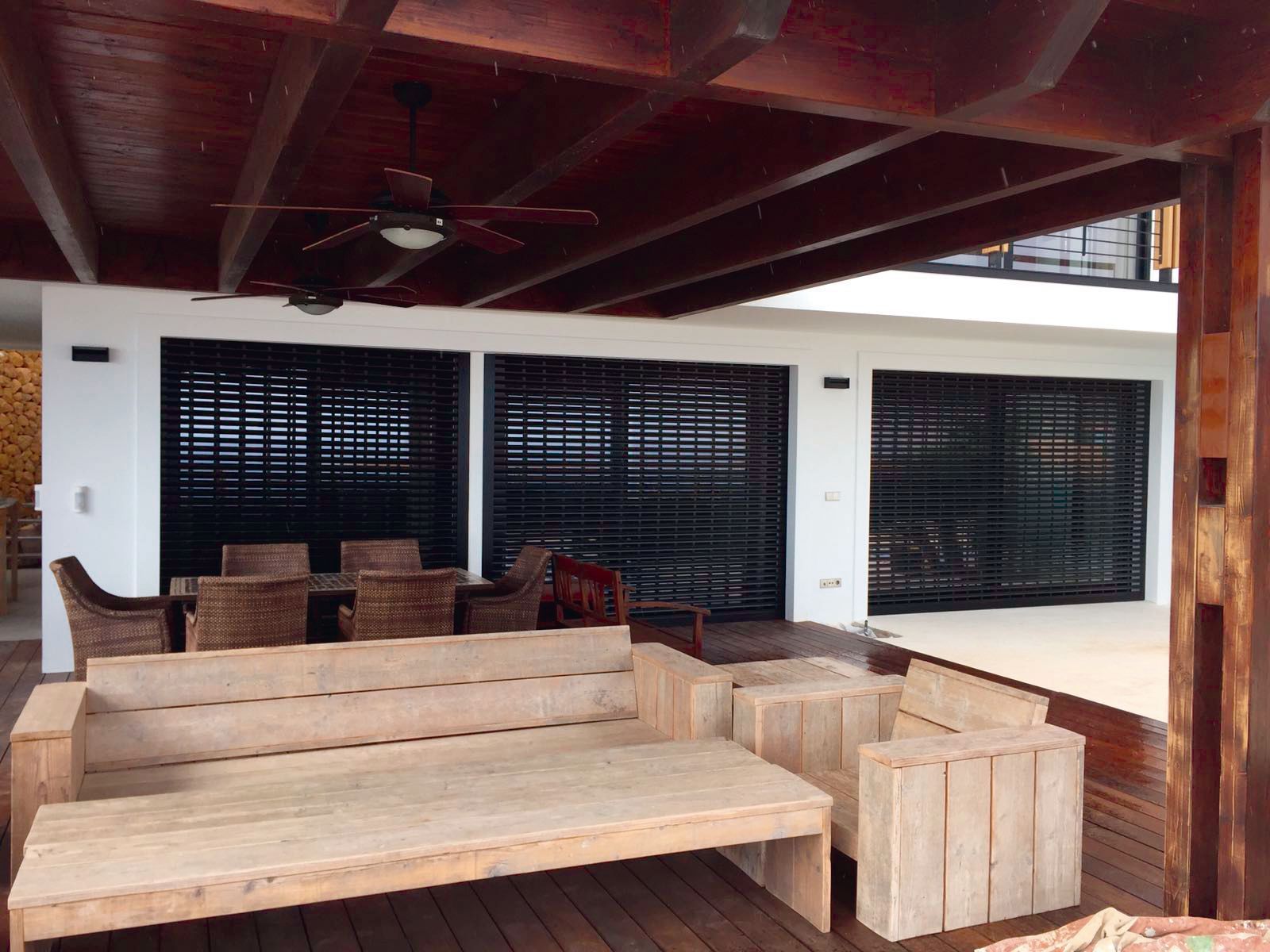 Una terraza de madera con un sofá y sillas debajo de un ventilador de techo.