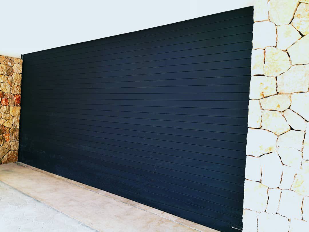 Una puerta de garaje negra está junto a una pared de piedra.