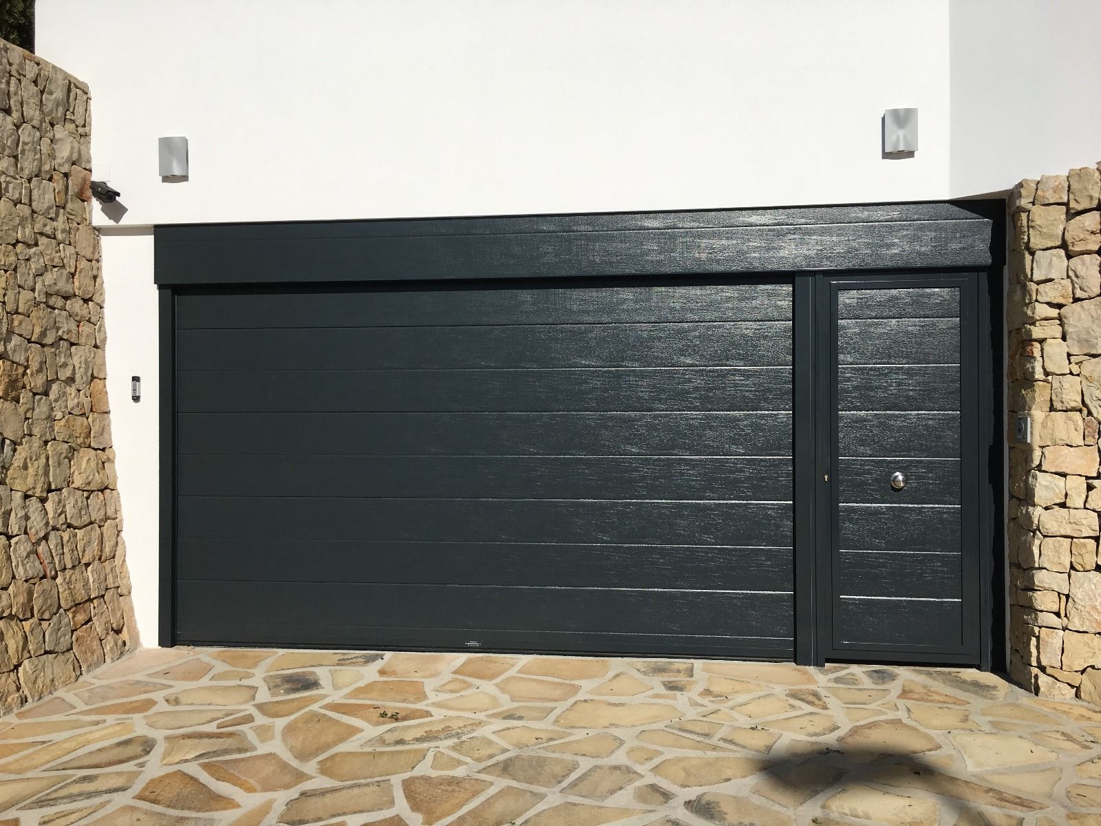 Una puerta de garaje negra está junto a una pared de piedra.