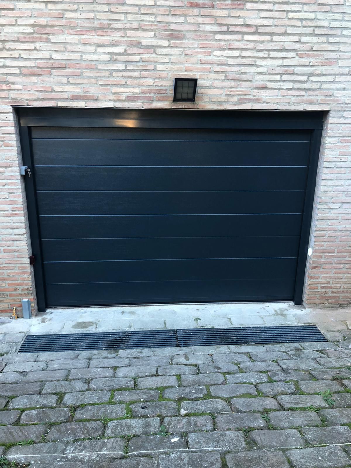 Una puerta de garaje negra está delante de un edificio de ladrillos.