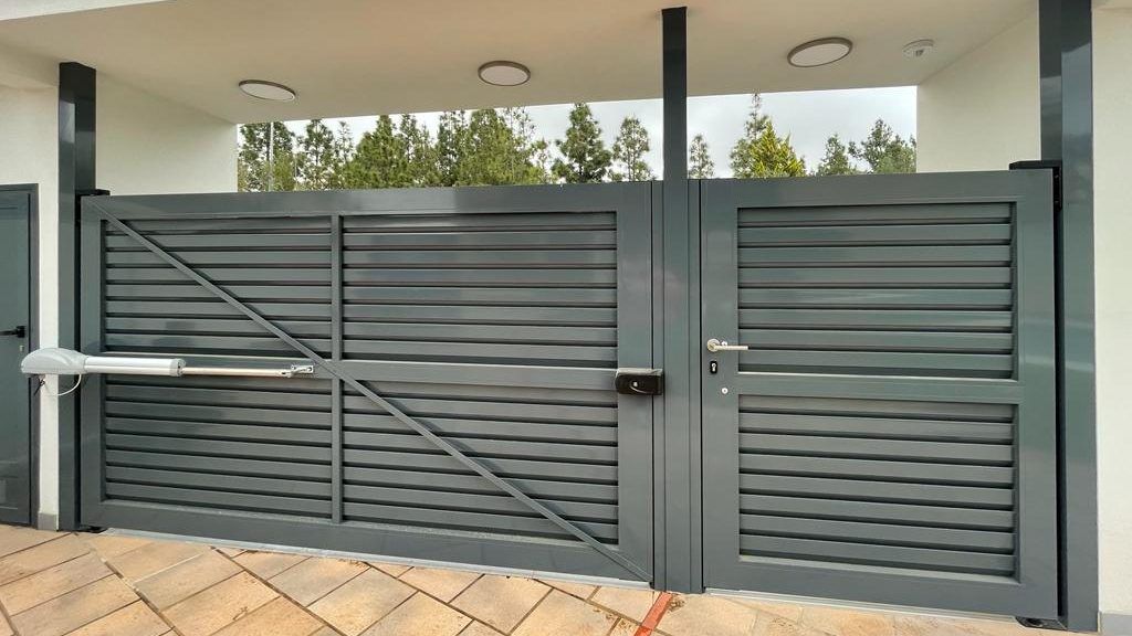 Una puerta de metal gris se abre y se cierra frente a un edificio.