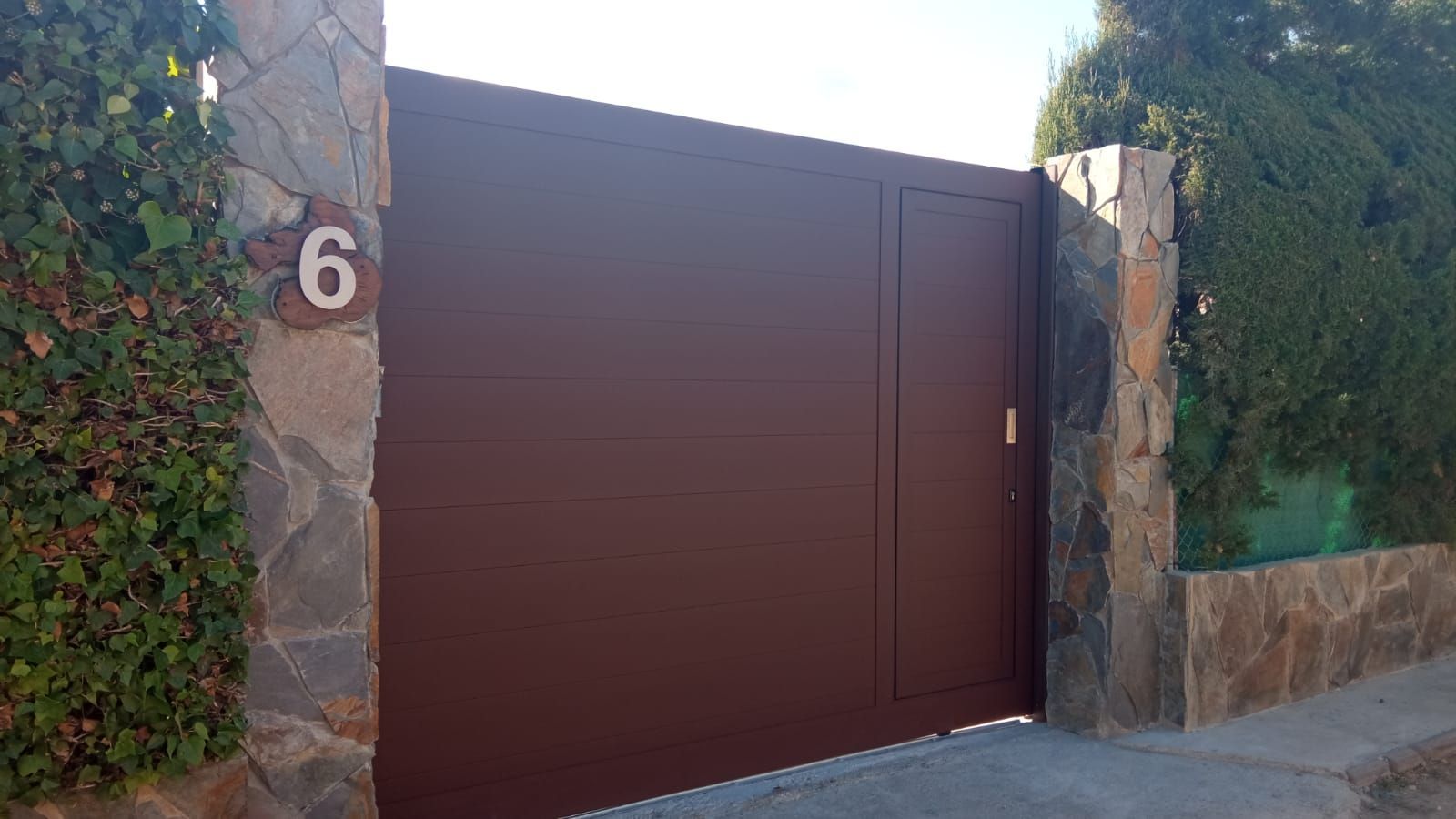 Una puerta marrón con el número 6 está al lado de un muro de piedra.
