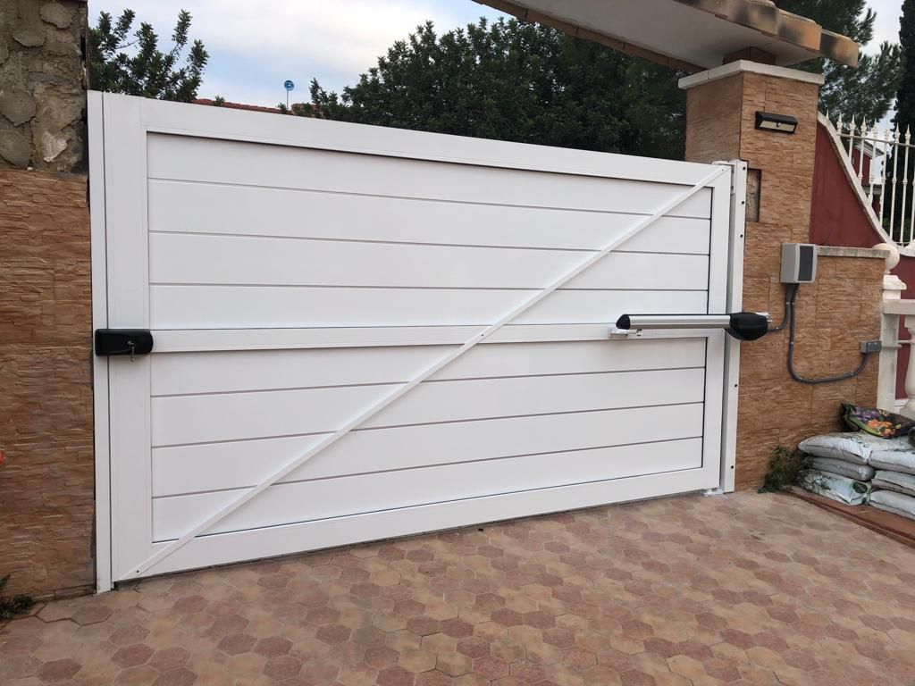 Una puerta blanca se abre a un camino de entrada al lado de una pared de ladrillos.