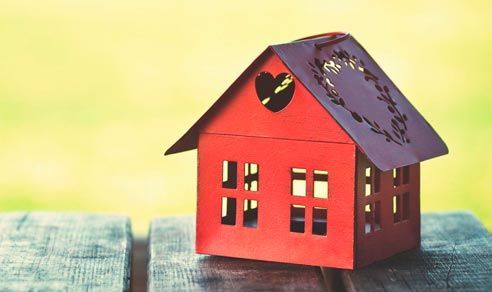 Una pequeña casa roja con un corazón en el techo está sentada sobre una mesa de madera.