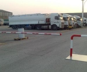 Una fila de camiones están estacionados en un estacionamiento detrás de una barrera roja y blanca.